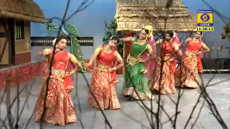 Dancers in vibrant costumes are gracefully moving on a stage, their hands and arms flowing in unison. A DD Odia logo is visible, indicating this is a performance from India.
