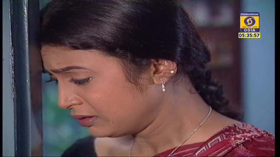 A woman leans against a wall, her face etched with sadness as tears stream down her cheek. The DD Odia logo in the corner shows it's a scene from a television drama.
