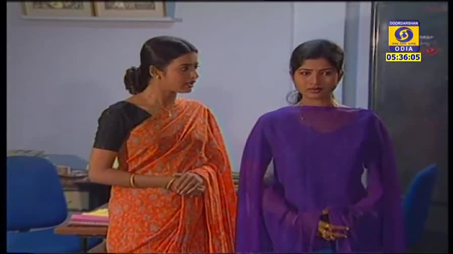 Two women stand facing each other, one in an orange sari, the other in a purple outfit. The DD Odia logo and the time are displayed in the corner.
