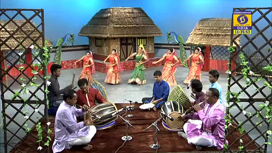 Dancers in vibrant costumes move gracefully on a stage, their movements mirroring the rhythm of the musicians playing traditional instruments. The DD Odia logo is visible, indicating a live broadcast from India.
