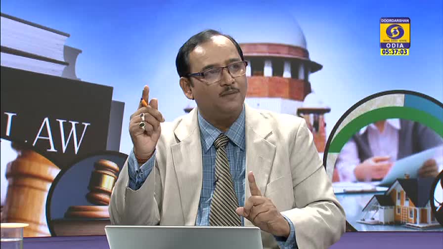 The man, wearing glasses and a light blazer, gestures with a pen as he speaks. Behind him, the DD Odia logo and a backdrop featuring the Supreme Court building are visible.
