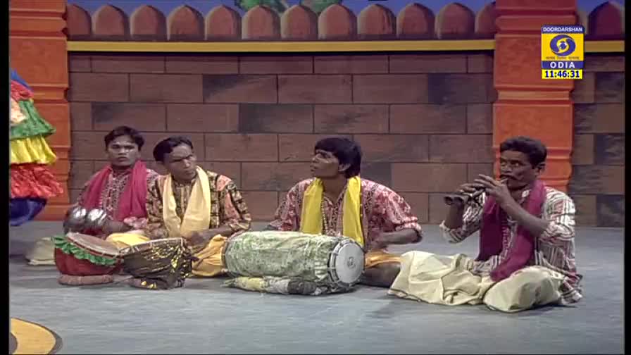 Four men sit on the floor, playing instruments: a drum, a flute, and what looks like a pair of small cymbals. The DD Odia logo is visible in the corner, and the time reads 11:46:31.
