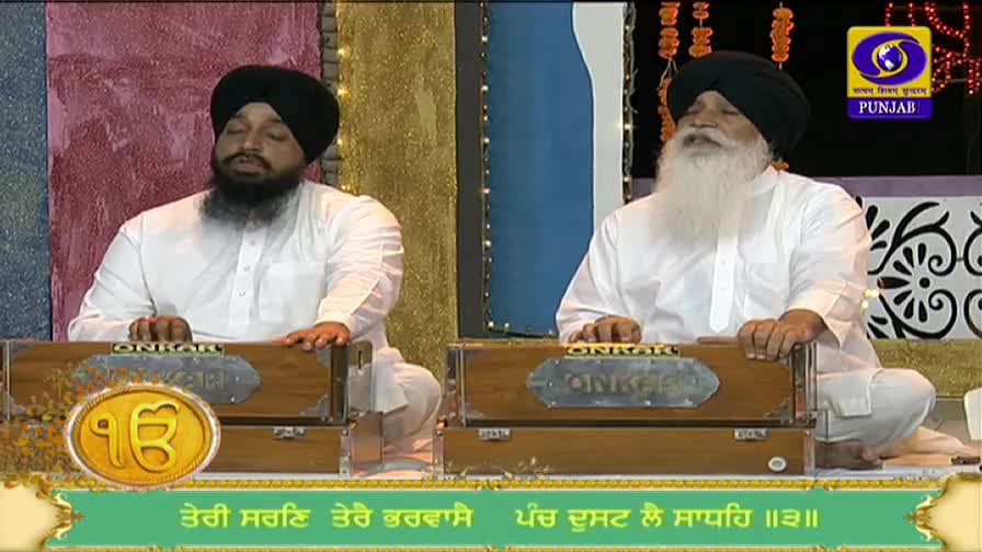 Two men in white tunics and turbans sit on a stage, their hands moving over wooden harmoniums. The DD Punjabi logo is visible in the corner, and a script runs along the bottom of the screen.
