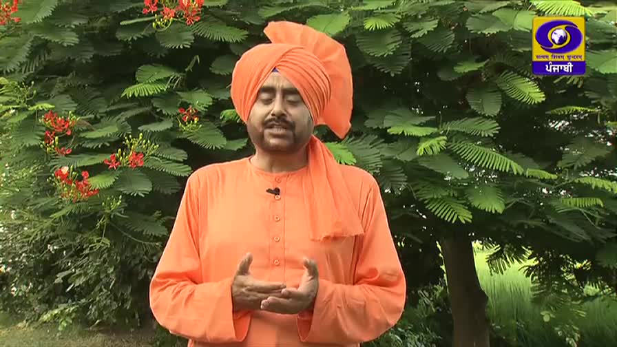 A man in an orange turban and robes stands before a lush green backdrop, gesturing with his hands. The DD Punjabi logo is visible in the upper right corner, indicating a broadcast from India.
