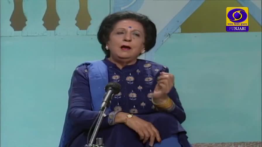 A woman in a blue outfit gestures with her right hand as she speaks into a microphone. The DD Punjabi logo is visible in the upper right corner.
