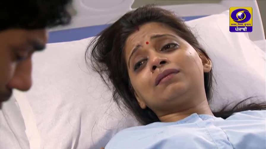 A woman lies in a hospital bed, tears tracing paths down her cheeks. A man's face is visible beside her, his expression somber as he looks down.
