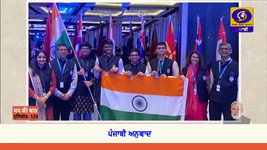 A group of people, some holding Indian flags, pose for a photo. The scene is framed by a DD Punjabi logo and a graphic from "Mann Ki Baat."
