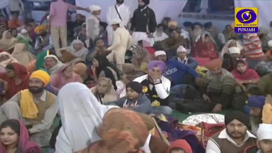 A large crowd sits on the ground, many wearing turbans and headscarves, gathered under a white canopy. The DD Punjabi logo indicates this is a broadcast from India.
