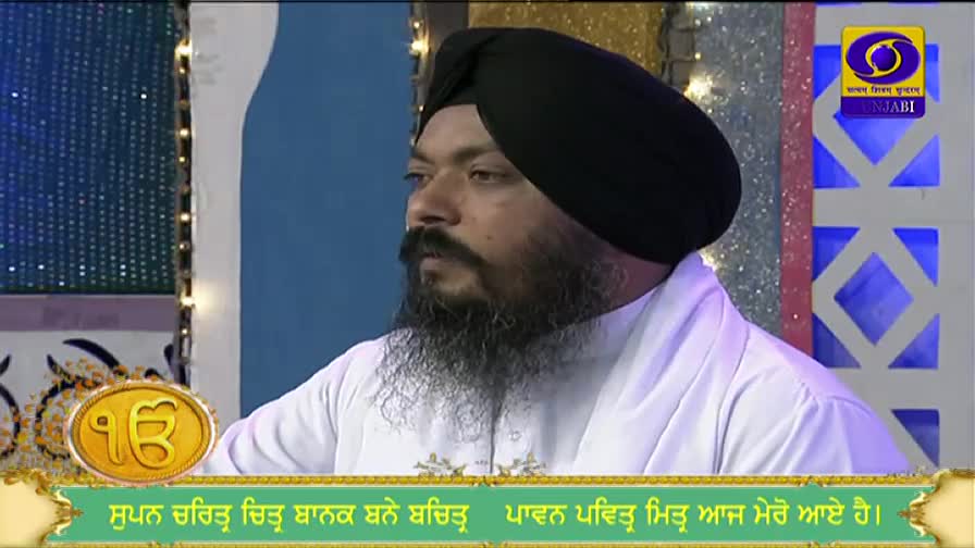 A man in a black turban and white robe is speaking, his gaze directed off-camera. The DD Punjabi logo and text in Punjabi are visible on the screen.
