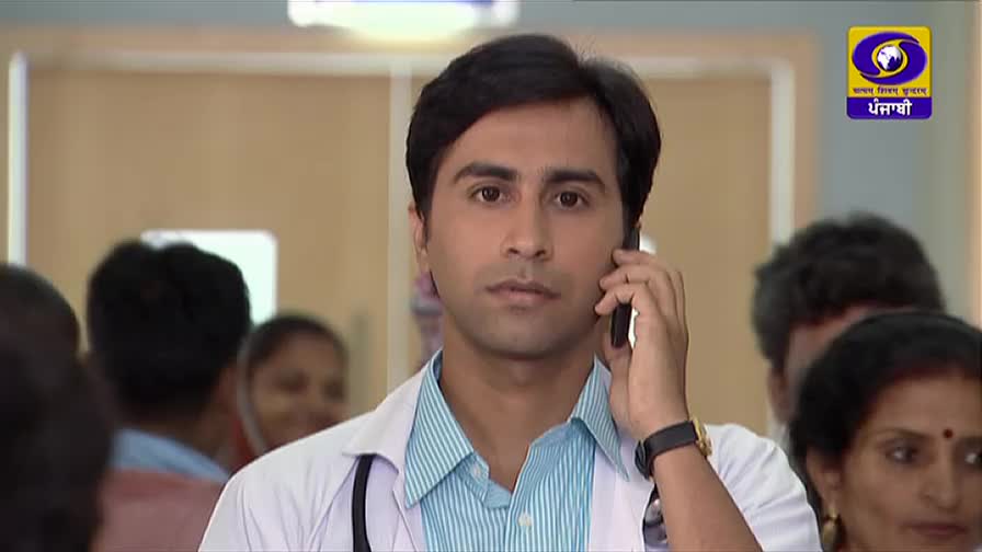 A doctor, wearing a white coat and stethoscope, is on the phone, his gaze focused. Behind him, a crowd of people stand in a brightly lit room, likely a hospital setting.
