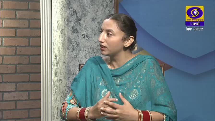 A woman in a teal salwar kameez gestures with her hands while speaking, her red bangles visible. The DD Punjabi logo is clear in the background.
