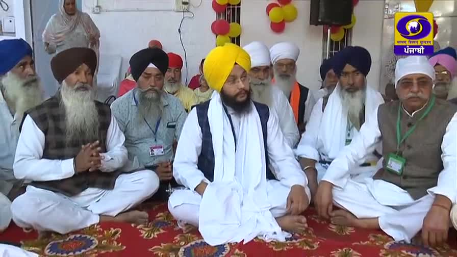 Men in turbans and traditional attire sit cross-legged on a patterned rug. A DD Punjabi logo is visible in the corner, suggesting a broadcast from India.
