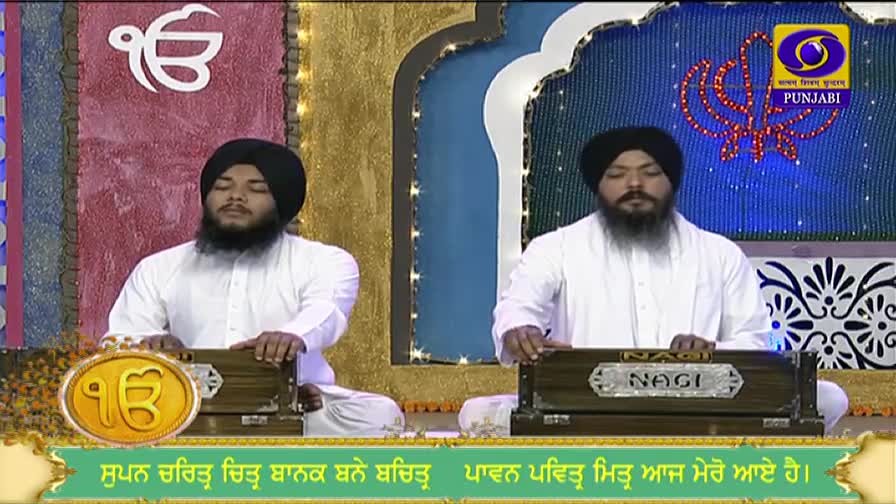 Two men, both in white, sit facing forward, their hands moving over the keys of small harmoniums. The DD Punjabi logo sits in the top right corner.
