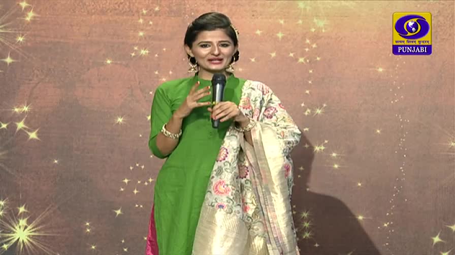 A woman in a bright green salwar kameez gestures with her hands, speaking into a microphone. The DD Punjabi logo is visible in the corner, and she's draped in a floral shawl.
