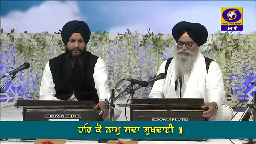 Two men in turbans sit side-by-side, each with a harmonium in front of them, singing into microphones. The DD Punjabi logo is visible in the corner, broadcasting from India.

