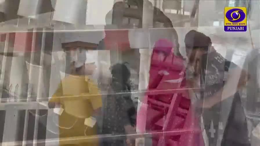 A woman in a vibrant pink head covering stands near a man wearing a turban, both appearing to be part of a scene broadcast on DD Punjabi. The image is overlaid with a series of vertical lines, creating a layered, almost ghostly effect.
