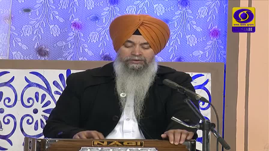 A man with a long white beard and an orange turban plays a harmonium, his fingers moving across the keys. The DD Punjabi logo is visible in the corner of the screen.