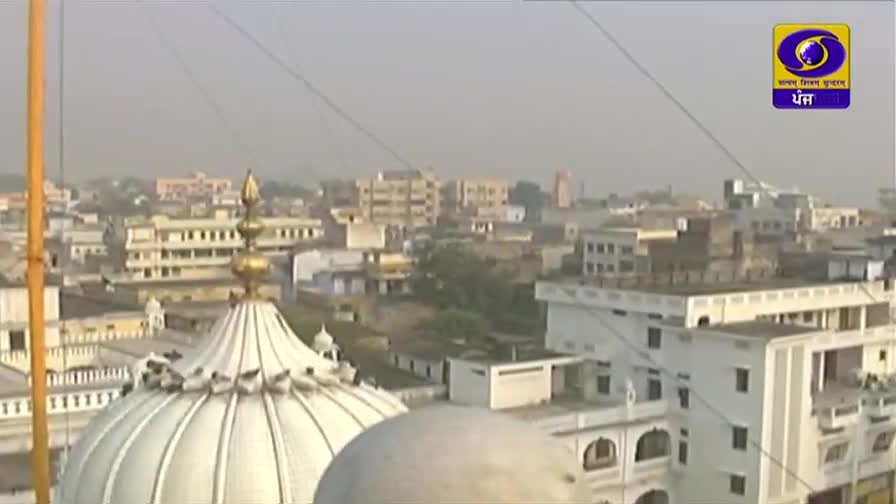 A golden spire crowns a white dome, its intricate design catching the light. Beyond, a hazy cityscape of Indian buildings stretches towards the horizon.