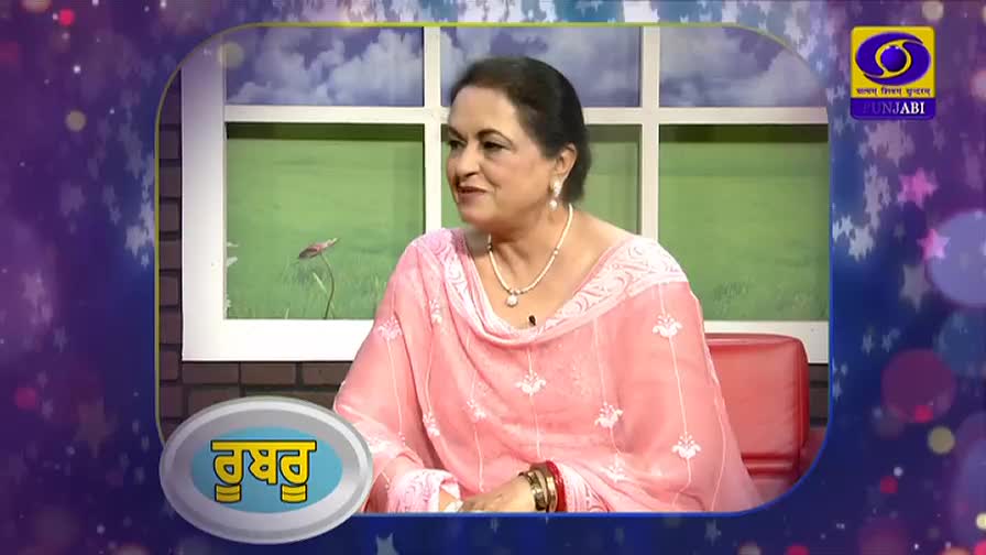 A woman in a pink salwar kameez sits on a red chair, speaking into a microphone. A logo for DD Punjabi is visible in the upper right corner.