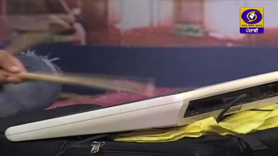 A hand grips a drumstick, poised to strike a white electronic drum pad. The DD Punjabi logo is visible in the background, suggesting a broadcast from India.