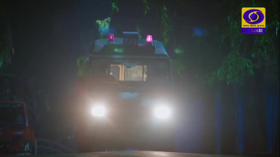 An ambulance with flashing red lights drives towards me on a dark road. Its headlights cut through the night, illuminating the path ahead.