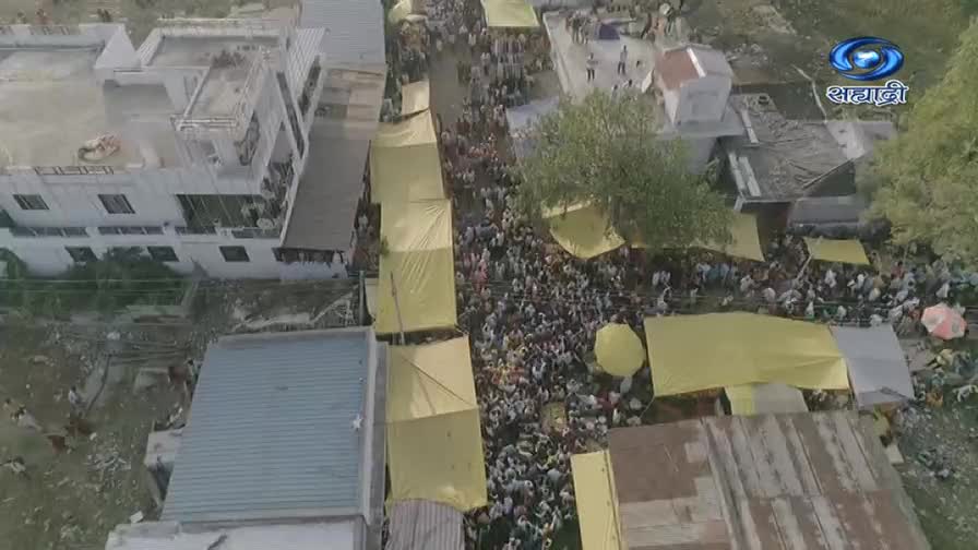 A packed street is shaded by yellow tarps, with a mass of people moving in both directions. The DD Sahyadri logo is in the corner, broadcasting the scene from India.
