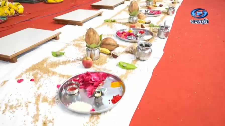 A long table is covered with a white cloth, scattered with grains and adorned with ritual items like coconuts, flowers, and small metal dishes. The DD Sahyadri logo is visible on the right, suggesting this is a broadcast of a traditional ceremony.
