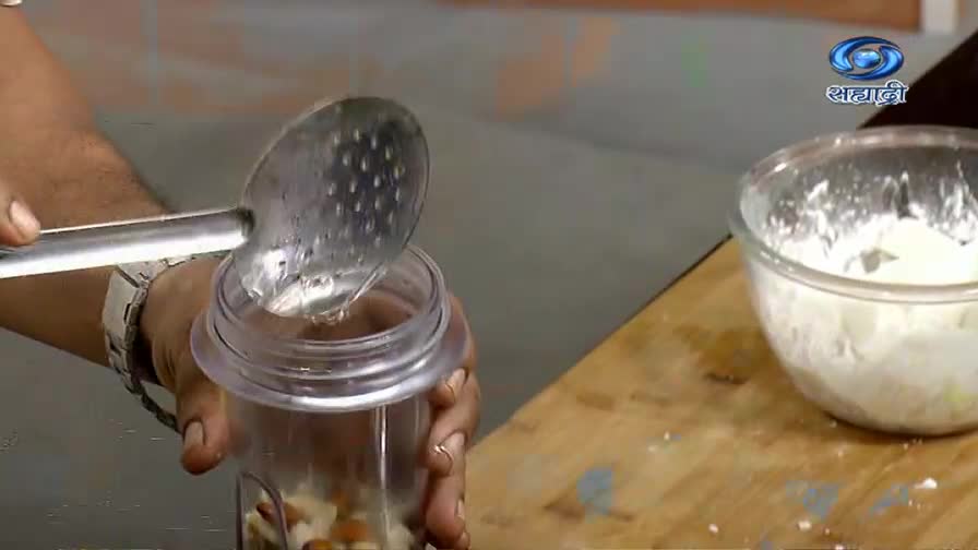 A slotted spoon pours liquid into a blender filled with nuts. The DD Sahyadri logo is visible in the upper right corner.
