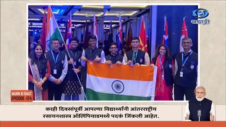 A group of people, some holding the Indian flag, pose for a photo. The DD Sahyadri logo is in the top right corner, and a man is speaking on a screen at the bottom.
