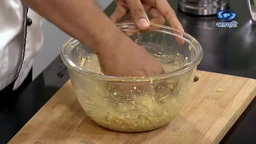 A cook's hands are submerged in a glass bowl, kneading a pale yellow mixture. The DD Sahyadri logo is visible in the corner, suggesting a cooking show.

