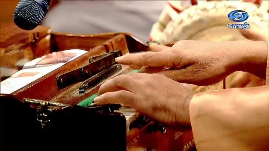 Fingers dance across the keys of a harmonium, the instrument's wooden frame catching the light. A microphone hovers above, ready to capture the music for DD Sahyadri.
