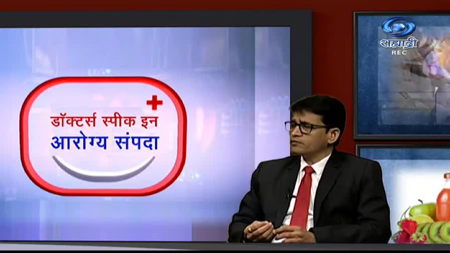 A man in a suit and tie sits in a studio on DD Sahyadri, looking towards the side. The screen behind him displays text in Hindi, and the channel's logo is in the corner.
