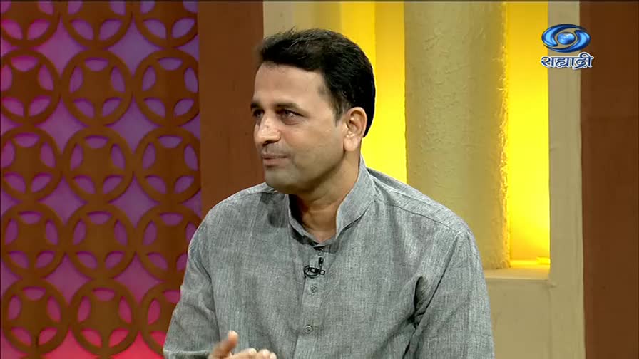 A man in a grey shirt is speaking, his gaze directed off-screen. The DD Sahyadri logo is visible in the corner, suggesting a television studio setting.
