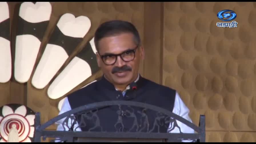 The man in glasses stands behind a podium, a microphone clipped to his lapel. The DD Sahyadri logo is visible in the corner, and he's looking directly at the camera.
