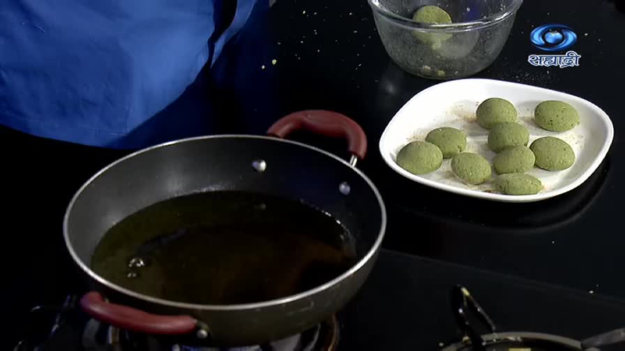 A pan of hot oil sits ready, while a plate of round, green dumplings waits nearby. The DD Sahyadri logo is visible in the background, suggesting a cooking demonstration.
A pan of hot oil sits ready, while a plate of round, green dumplings waits nearby. The DD Sahyadri logo is visible in the background, suggesting a cooking demonstration.