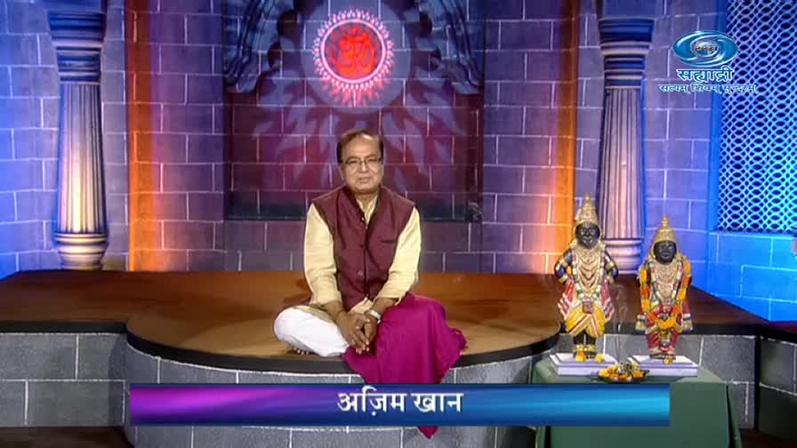 A man in a vest and glasses sits cross-legged on a circular platform, framed by a brick wall and pillars. Two small statues stand on a table, and the DD Sahyadri logo is visible in the corner.
