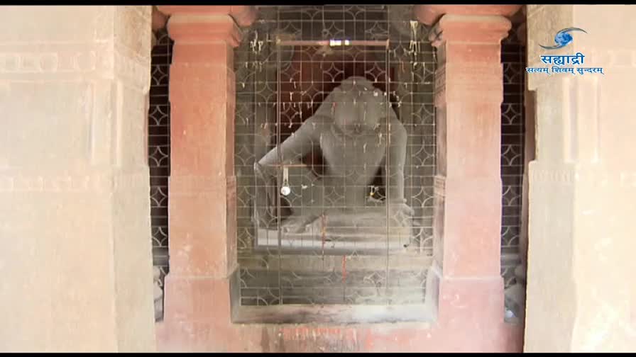 A stone statue of a figure, behind a metal grate, is framed by the pink columns of a building. The DD Sahyadri logo sits in the upper right corner.
