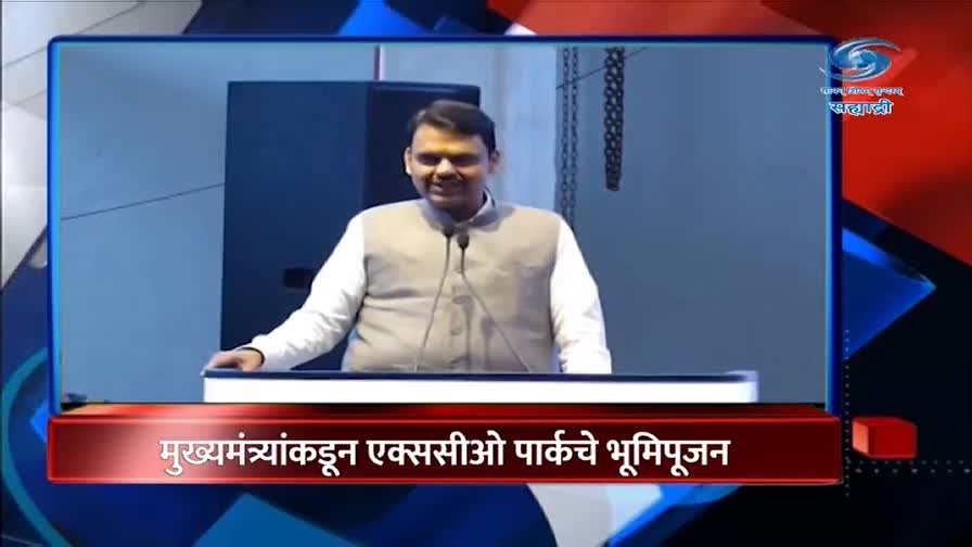 A man in a grey vest over a white shirt stands at a podium, speaking into microphones. A red banner at the bottom of the screen, in Marathi, announces an event related to the Chief Minister.
