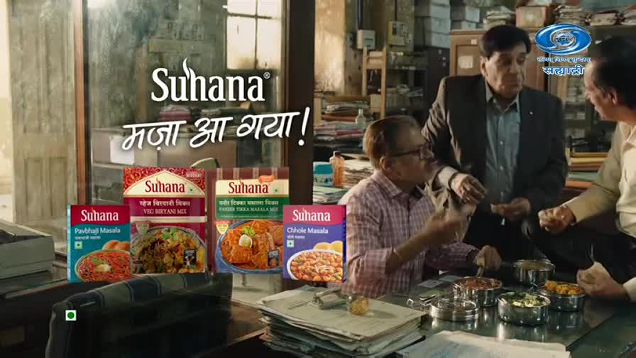 Three men are gathered around a table, looking at food containers. The Suhana brand logo and Hindi text are prominently displayed. Three men are gathered around a table, looking at food containers. The Suhana brand logo and Hindi text are prominently displayed.