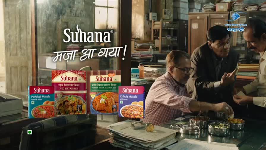 Three men are gathered around a desk in what looks like an office, with several small metal tiffin containers and boxes of Suhana masalas. One man is pointing at something on the desk while another looks on intently. The DD Sahyadri logo is visible in the background. Three men are gathered around a desk in what looks like an office, with several small metal tiffin containers and boxes of Suhana masalas. One man is pointing at something on the desk while another looks on intently. The DD Sahyadri logo is visible in the background.