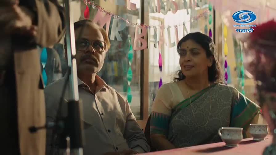 A man in glasses and a woman in a sari sit at a table, a festive banner strung behind them. The DD Sahyadri logo is visible in the upper right corner.