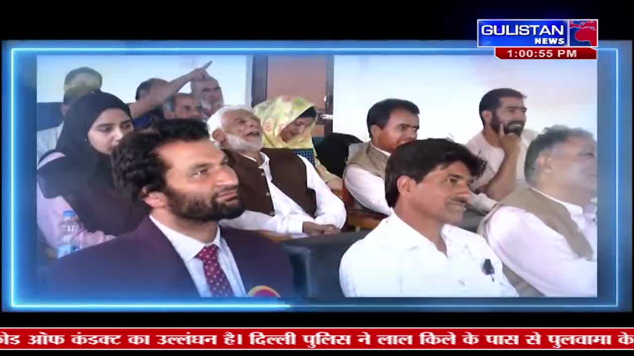 A group of men and women are seated, looking towards something off-camera. One man in the foreground, wearing a maroon suit and a patterned tie, turns his head to the side with a slight smile. In the background, a man in a white shirt and brown vest laughs heartily.