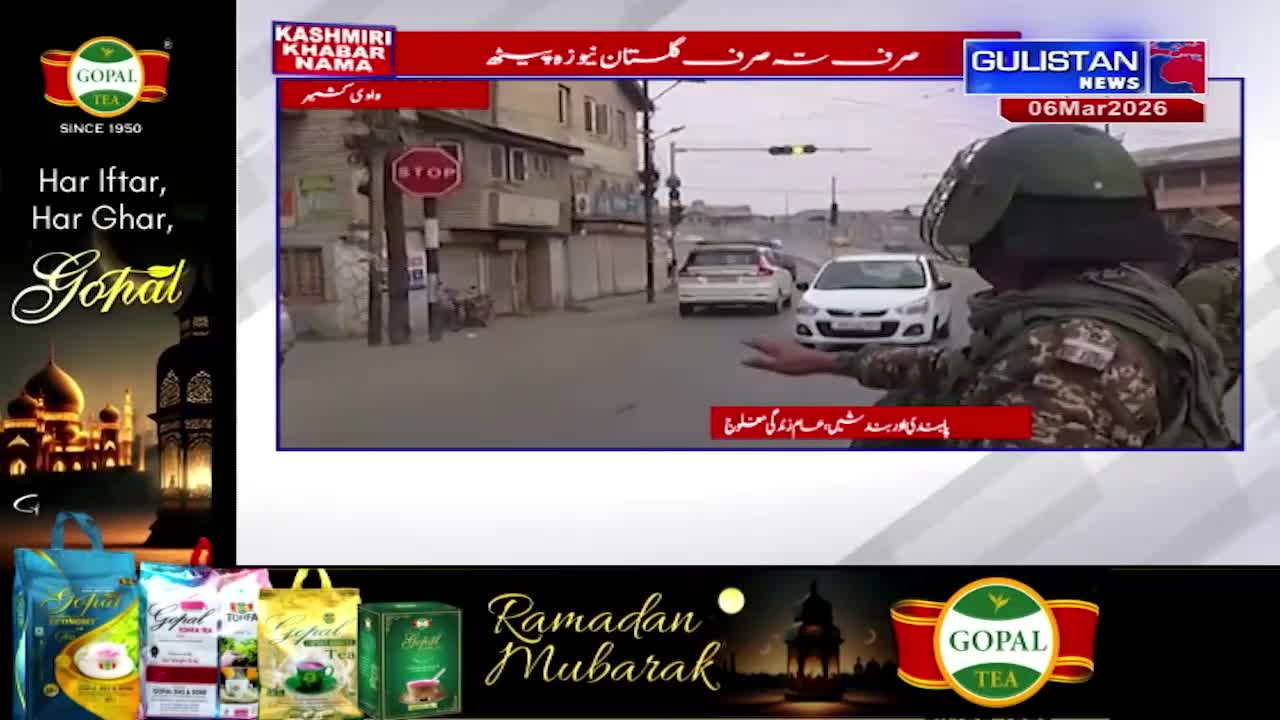 A soldier in a helmet signals traffic to stop on a street in Kashmir. Cars are lined up, waiting for clearance.