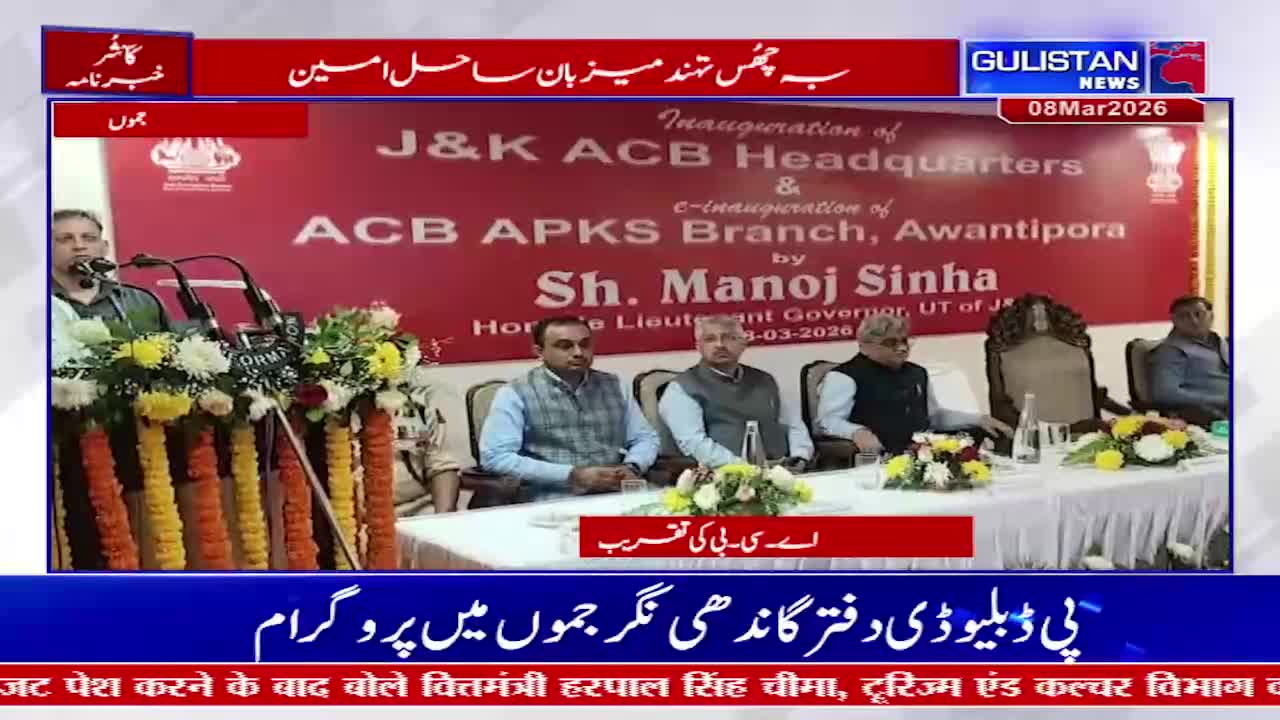 A man stands at a podium, speaking into a microphone. On a table before him, several men in formal attire are seated, listening. A large banner behind them announces the inauguration of J&K ACB Headquarters and ACB APKS Branch, Awantipora, by Sh. Manoj Sinha, Hon'ble Lieutenant Governor, UT of J&K.