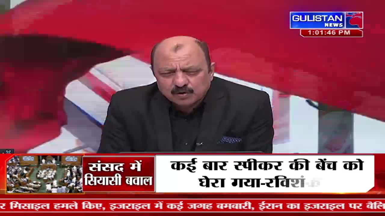 A man in a black suit speaks intently, his face framed by a red backdrop. Below him, a news ticker scrolls with Hindi text, mentioning "Parliamentary debate" and "missile attacks."