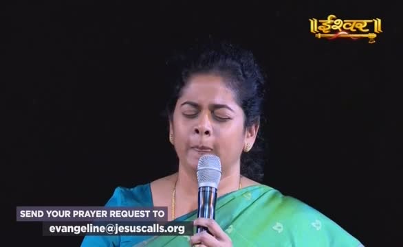 A woman in a green sari holds a microphone, eyes closed, as if in prayer. The Ishwar Bhakti TV logo is visible in the top right corner, and a request for prayer is displayed at the bottom.
