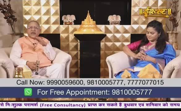 A man in a peach-colored vest gestures with his hands while speaking, as the woman next to him in a blue sari sits quietly. The Ishwar Bhakti TV logo sits proudly above the set.
