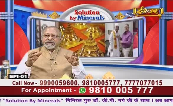 A man in a tan vest gestures with both hands, speaking on what looks like a TV show from India. Behind him, a screen shows a glimpse of what appears to be a religious ceremony, with two men in traditional clothing.
