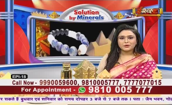 The woman on Ishwar Bhakti TV is in a pink and gold sari, speaking directly to the camera. Behind her, a bracelet made of blue and white stones is displayed alongside other objects, all under the banner "Solution by Minerals."
