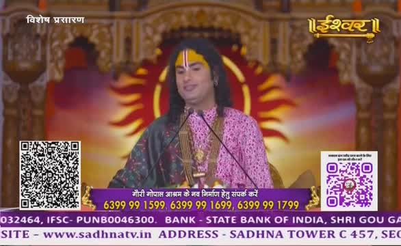A man in a pink and green patterned outfit speaks into two microphones, his words likely broadcast on Ishwar Bhakti TV in India. Behind him, a large sun-like design glows, and QR codes flank the bottom of the screen.
